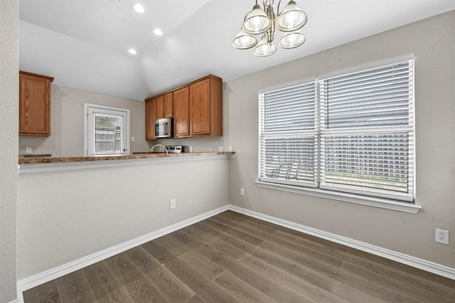 kitchen with dark wood finished floors, stainless steel microwave, brown cabinetry, vaulted ceiling, and baseboards