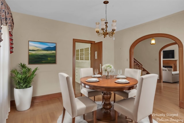 dining area with arched walkways, light wood-style flooring, a notable chandelier, baseboards, and stairs