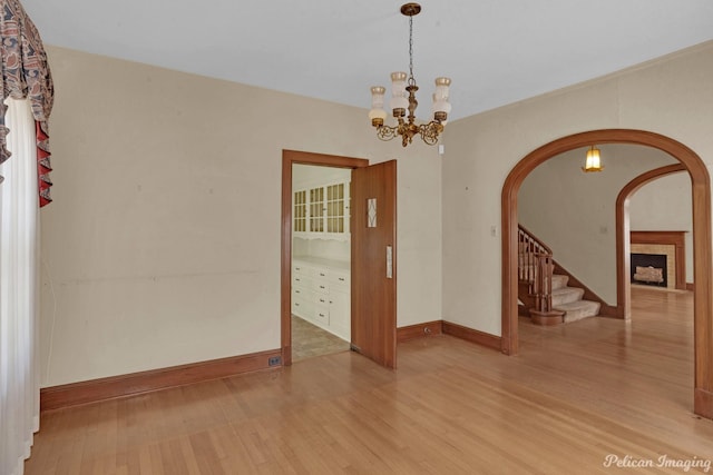 unfurnished room with stairs, arched walkways, a chandelier, and wood finished floors