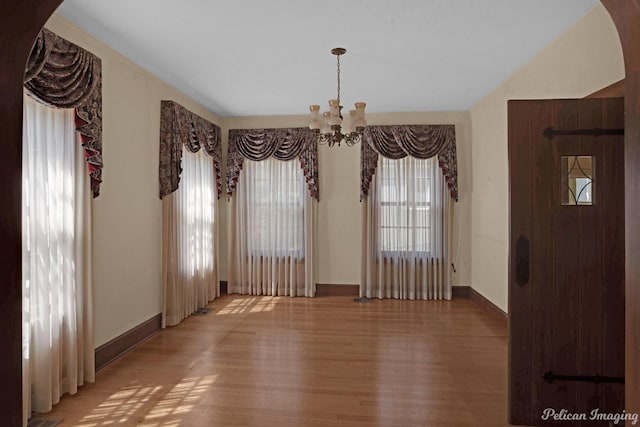 unfurnished dining area featuring a chandelier, arched walkways, baseboards, and wood finished floors