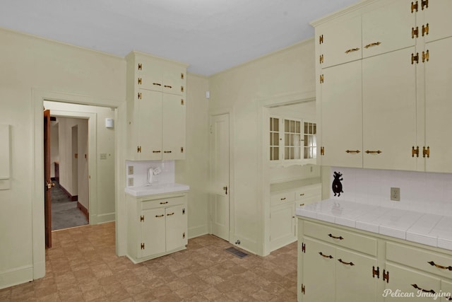 kitchen featuring crown molding, light floors, tile counters, visible vents, and backsplash