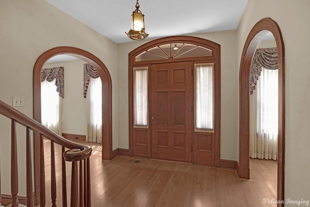 entryway featuring arched walkways, plenty of natural light, stairs, and light wood-style floors