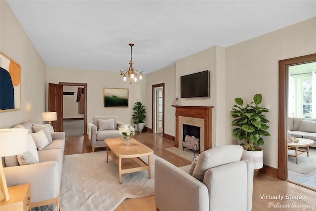 living area with a fireplace with flush hearth, baseboards, light wood finished floors, and an inviting chandelier