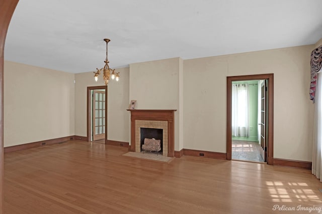 unfurnished living room featuring an inviting chandelier, baseboards, a tiled fireplace, and wood finished floors