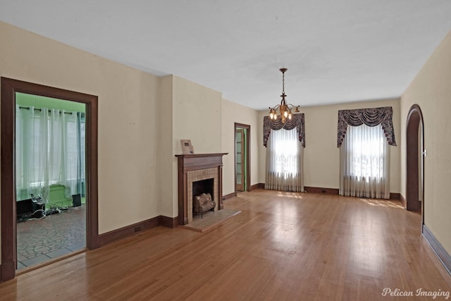 unfurnished living room featuring baseboards, a fireplace, wood finished floors, and a notable chandelier