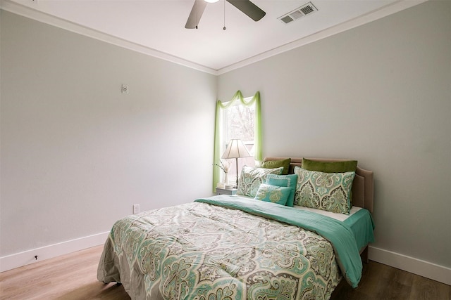 bedroom with visible vents, ornamental molding, ceiling fan, wood finished floors, and baseboards