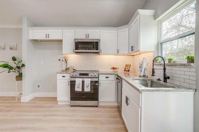 kitchen featuring appliances with stainless steel finishes, light stone countertops, light wood-type flooring, white cabinetry, and a sink