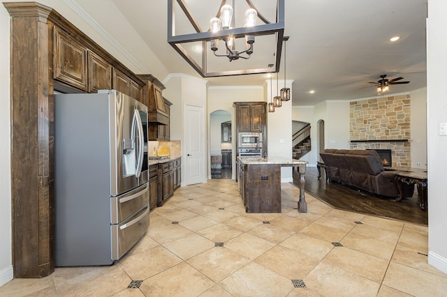 kitchen featuring arched walkways, appliances with stainless steel finishes, ornamental molding, open floor plan, and dark brown cabinets