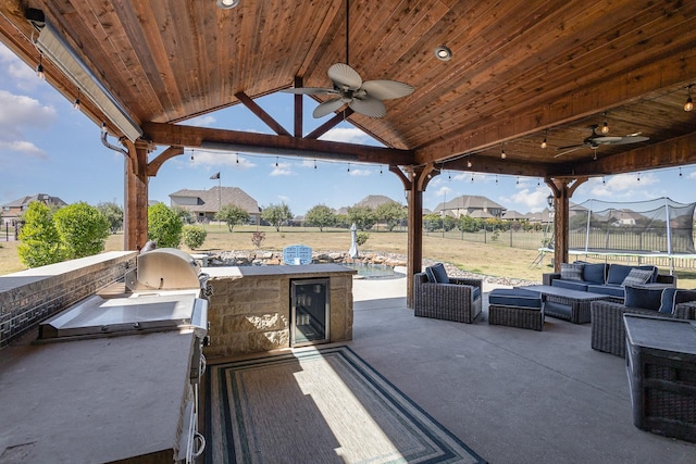 view of patio with beverage cooler, a trampoline, an outdoor living space, and a ceiling fan