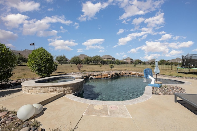 view of swimming pool with a pool with connected hot tub, a trampoline, fence, and a patio