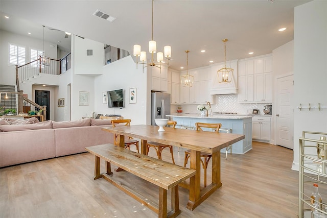 dining space with visible vents, light wood-style flooring, stairway, an inviting chandelier, and a high ceiling