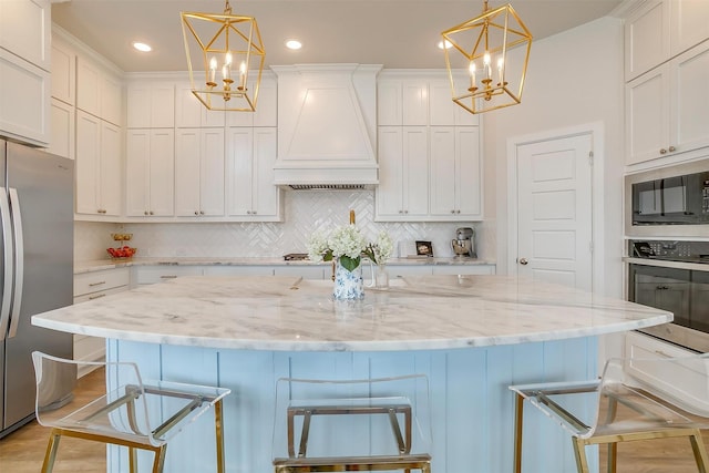 kitchen featuring appliances with stainless steel finishes, a chandelier, custom range hood, and white cabinets