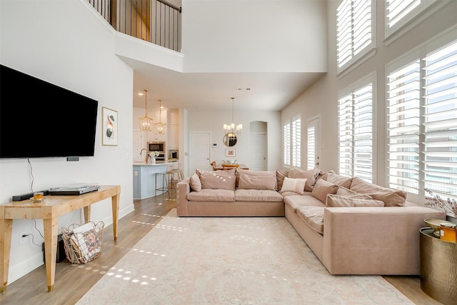 living room with baseboards, light wood-style floors, a high ceiling, and an inviting chandelier