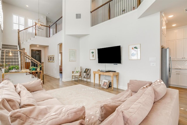 living room featuring light wood-type flooring, visible vents, baseboards, and stairs