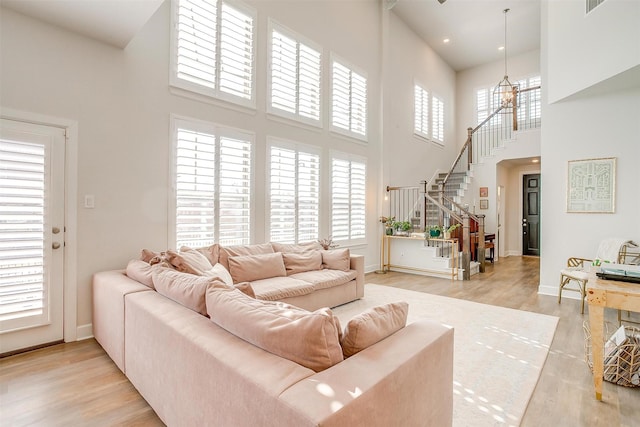 living area featuring stairs, a towering ceiling, light wood-style flooring, and baseboards