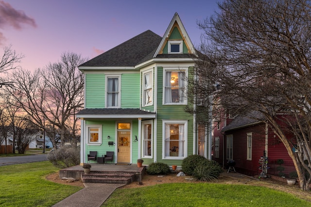 view of front of home with covered porch, a front lawn, and roof with shingles