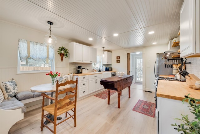 kitchen featuring pendant lighting, light wood finished floors, white cabinetry, a sink, and wood counters