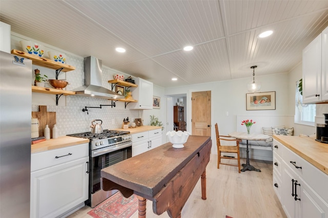 kitchen with stainless steel appliances, open shelves, white cabinetry, wooden counters, and wall chimney exhaust hood