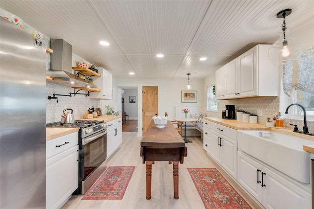 kitchen featuring stainless steel appliances, a sink, butcher block countertops, light wood-type flooring, and wall chimney exhaust hood