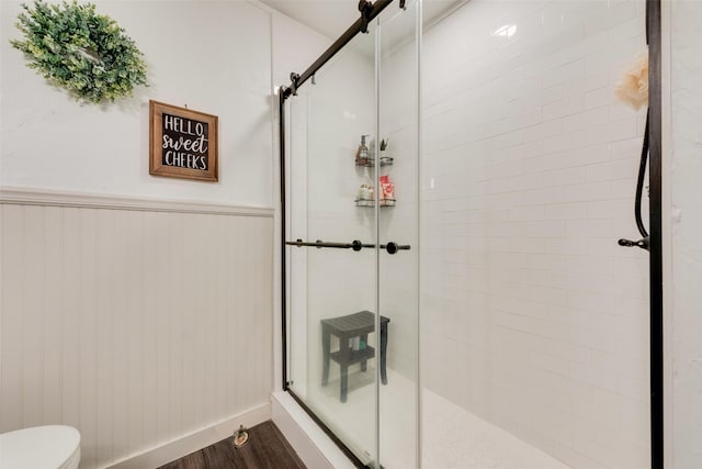 bathroom featuring toilet, a stall shower, a wainscoted wall, and wood finished floors