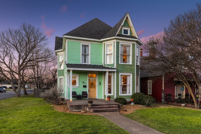 victorian house with covered porch, a shingled roof, and a lawn