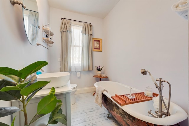 bathroom featuring baseboards, a freestanding bath, toilet, and wood finished floors