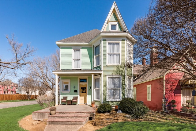 view of front of home featuring a porch, a front lawn, a shingled roof, and fence