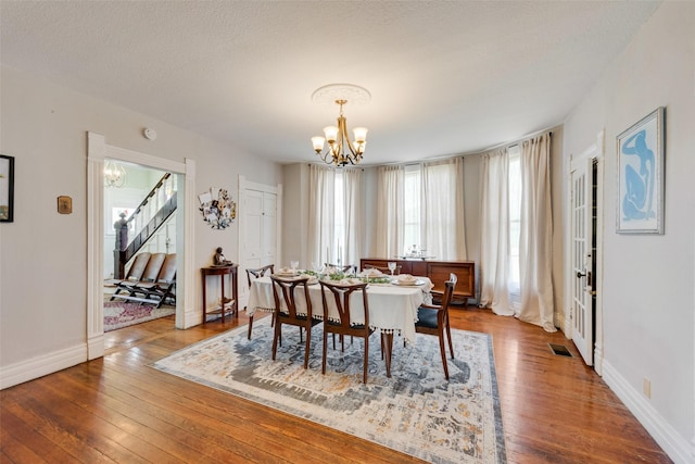 dining area with hardwood / wood-style flooring, stairway, visible vents, and a notable chandelier