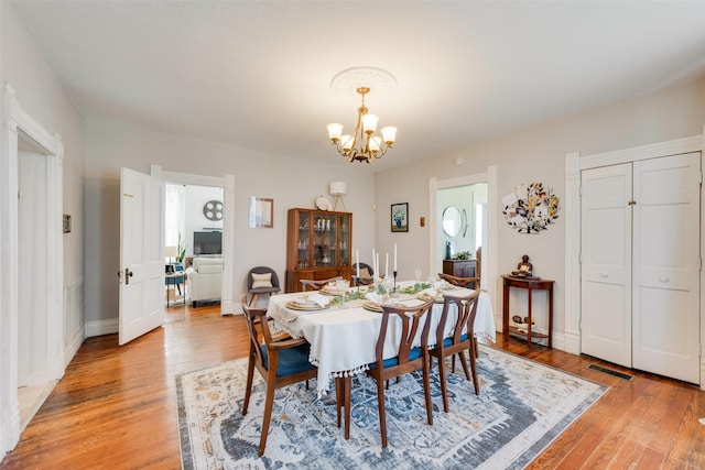 dining space featuring light wood-style floors, baseboards, visible vents, and a chandelier