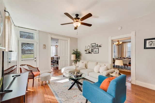 living area with baseboards, ceiling fan with notable chandelier, light wood-style flooring, and a healthy amount of sunlight