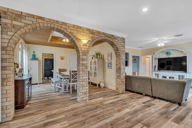 living room featuring a ceiling fan, arched walkways, ornamental molding, and light wood finished floors