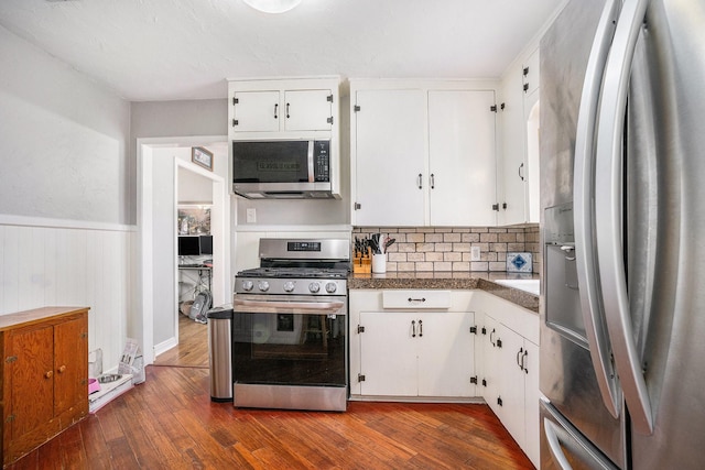 kitchen featuring a wainscoted wall, white cabinets, appliances with stainless steel finishes, dark countertops, and dark wood finished floors