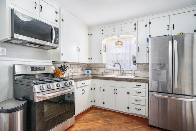 kitchen with white cabinets, dark wood finished floors, decorative backsplash, stainless steel appliances, and a sink