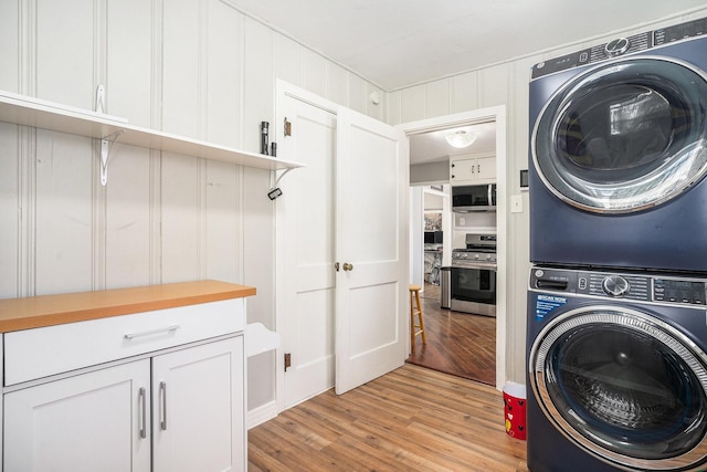 laundry room with stacked washer and dryer, cabinet space, and light wood finished floors