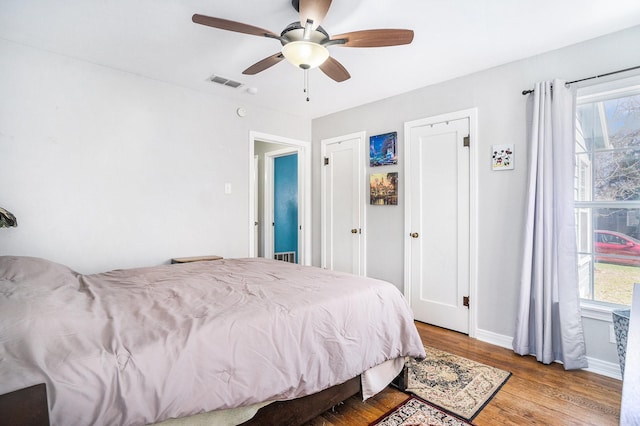 bedroom with ceiling fan, wood finished floors, visible vents, and baseboards