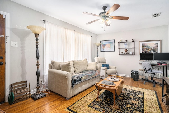 living room featuring a ceiling fan, visible vents, baseboards, and wood finished floors