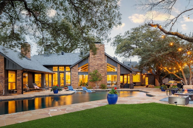 rear view of house with a patio, a shingled roof, a yard, an outdoor pool, and a chimney