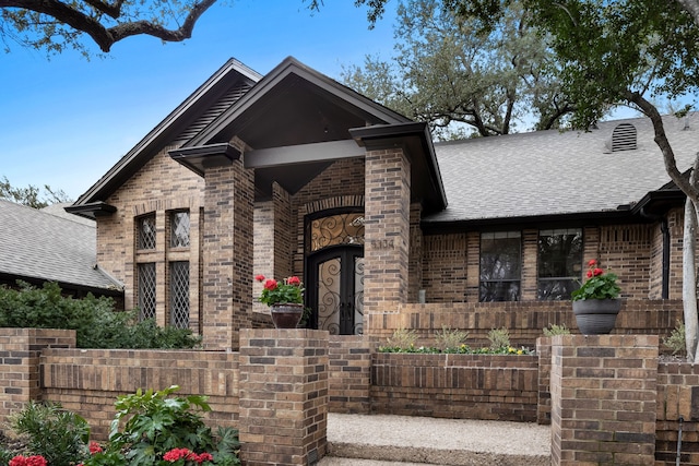 view of front of home featuring covered porch, brick siding, and roof with shingles