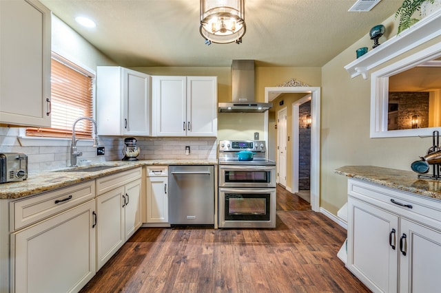 107 S Graves St, Mckinney, TX 75069 - kitchen featuring appliances with stainless steel finishes, wall chimney range hood, a sink, decorative backsplash, and white cabinetry