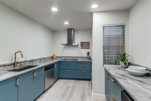 kitchen with blue cabinets, a sink, stainless steel dishwasher, wall chimney range hood, and light wood finished floors