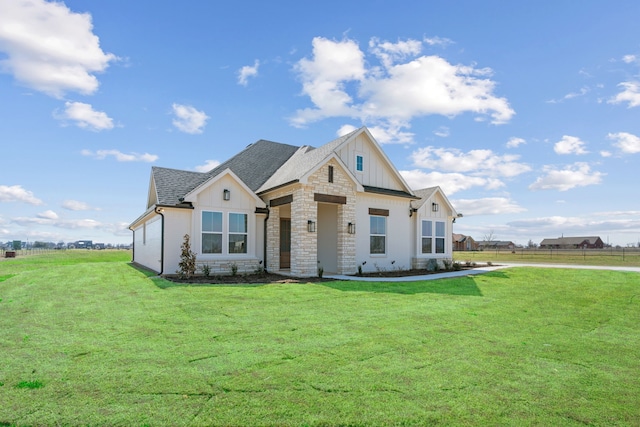 modern farmhouse style home with board and batten siding, a front yard, stone siding, and a shingled roof