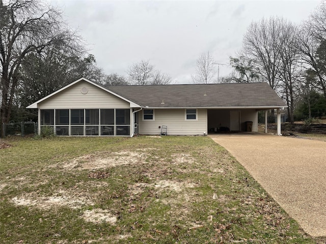 rear view of house with an attached carport, concrete driveway, a yard, and a sunroom