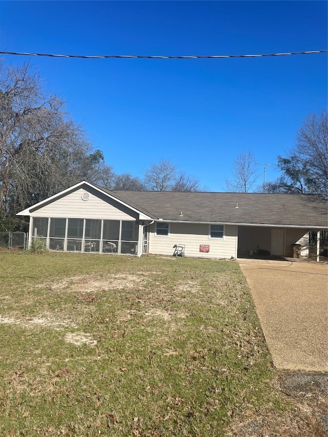 rear view of house featuring a carport, concrete driveway, a lawn, and a sunroom