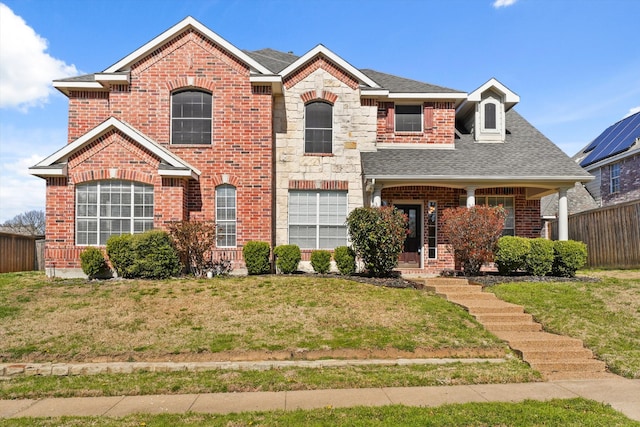 view of front of house with a front lawn, stone siding, fence, roof with shingles, and brick siding