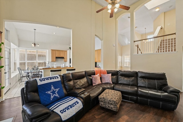 living area featuring a high ceiling, hardwood / wood-style floors, and ceiling fan with notable chandelier