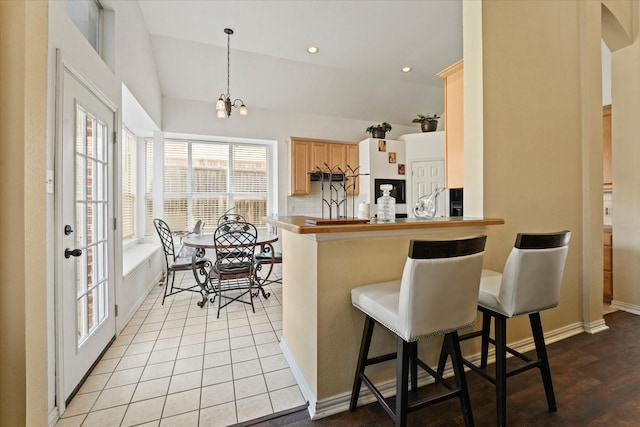 kitchen featuring light brown cabinetry, lofted ceiling, recessed lighting, a kitchen breakfast bar, and light tile patterned flooring