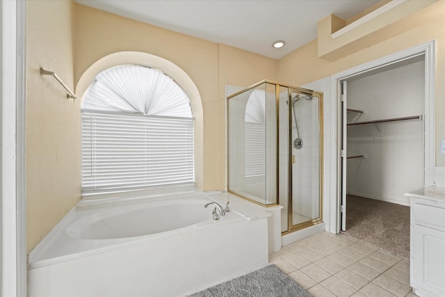 bathroom with tile patterned floors, a stall shower, a bath, a walk in closet, and vanity