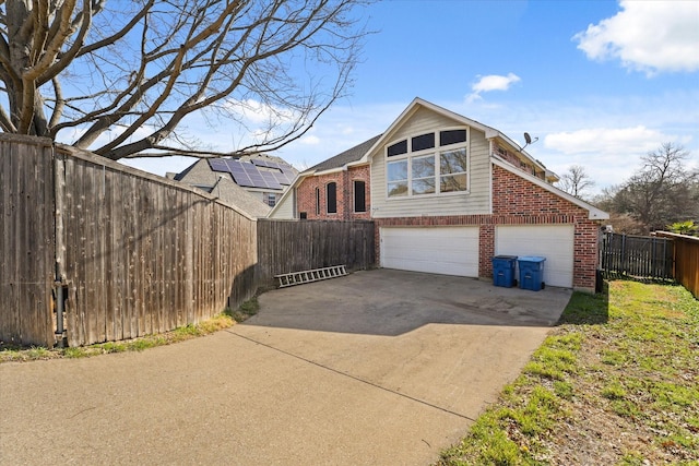 view of front of house featuring brick siding, concrete driveway, and fence