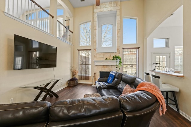 living room featuring baseboards, dark wood-type flooring, a high ceiling, and a fireplace