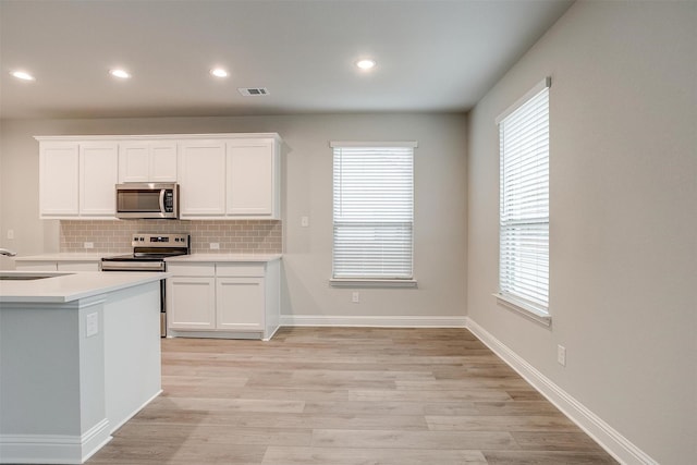 kitchen featuring stainless steel appliances, visible vents, decorative backsplash, white cabinets, and light wood-type flooring